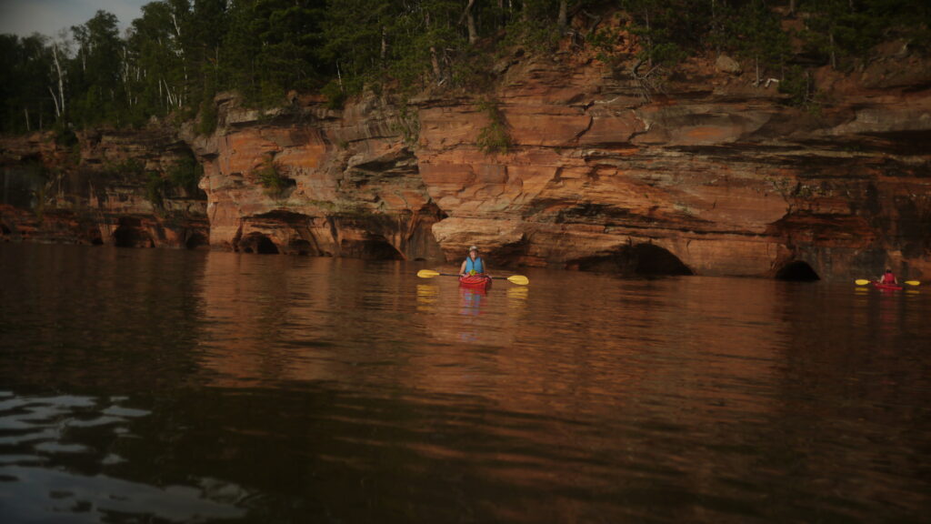 A woman is kayaking near sea caves in Bayfield, WI