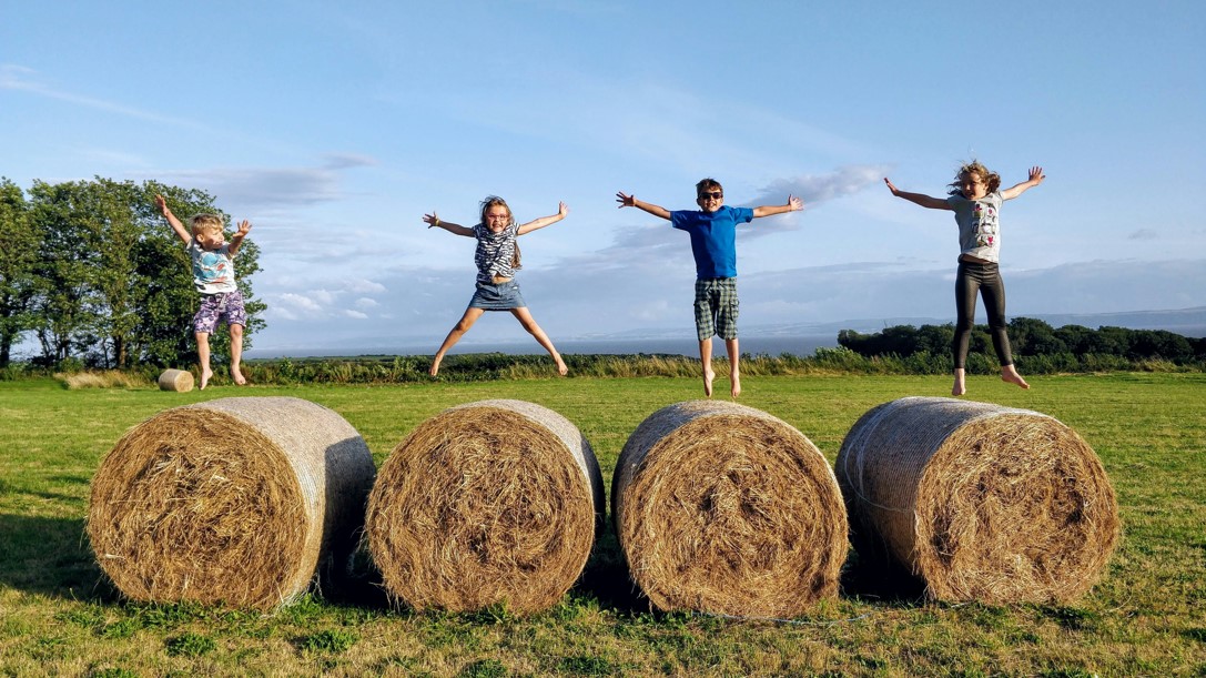 Four kids jumping on hay on a farm in New Hampshire