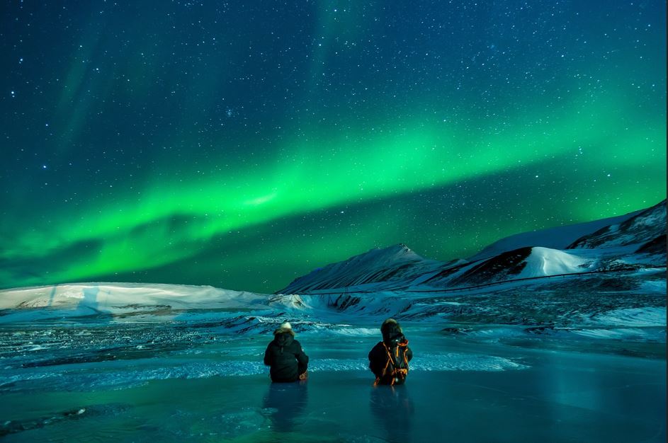 Two fisherman watch the Northern Lights as they fish at night.