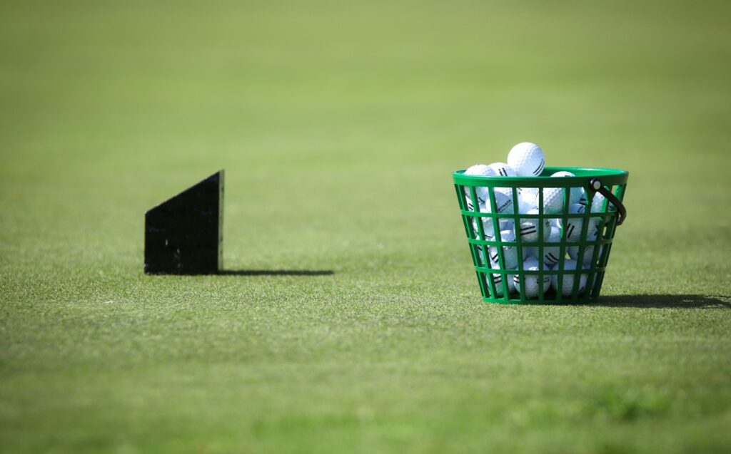 A bucket of golf balls sits in a green basket on the fairway.