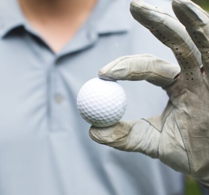 Golfer holds golf ball with his thumb and forefinger.