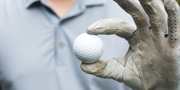 Golfer holds golf ball with his thumb and forefinger.