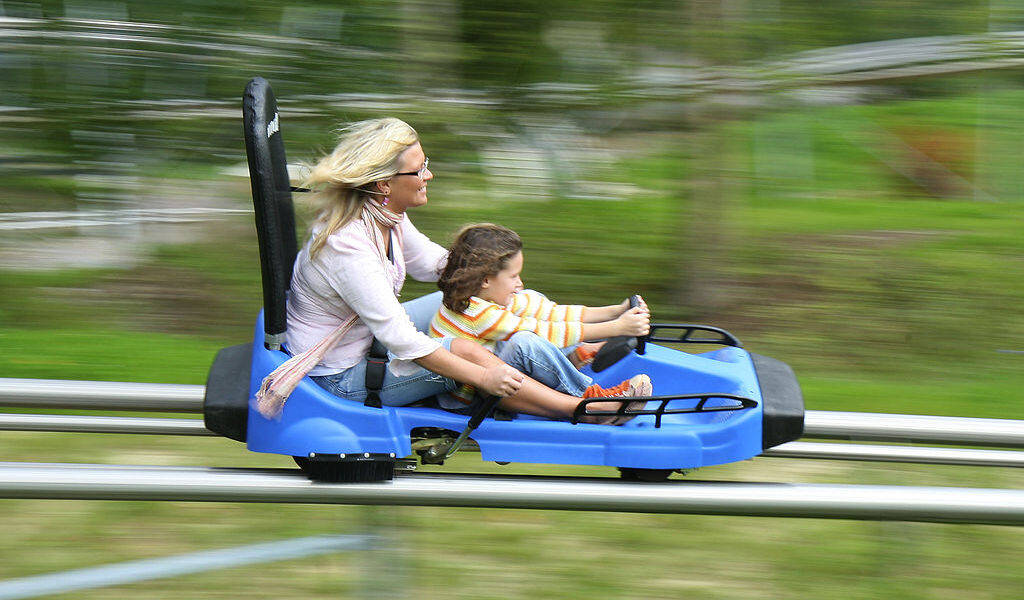 A mother and child zip down a popular mountain coaster- their hair blowing in the wind due to their speed.