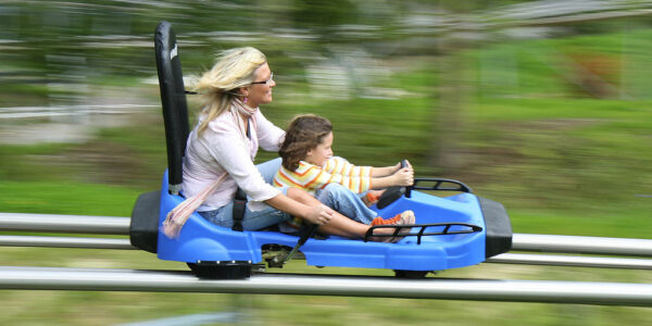 A mother and child zip down a popular mountain coaster- their hair blowing in the wind due to their speed.