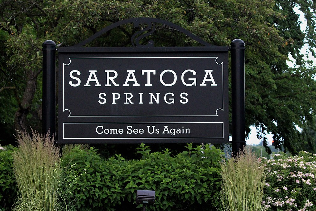 A sign at the edge of the town of Saratoga Springs encourages visitors to come again.