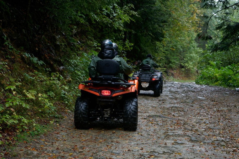 Two ATVs race down a dirt path in the forest.