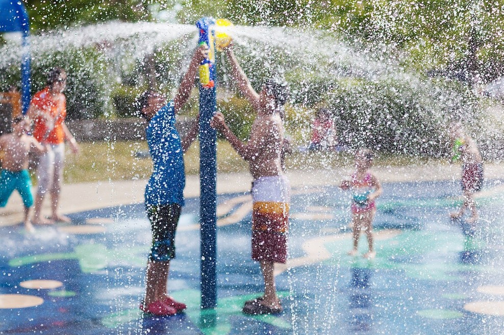 Two children reach up into a spray of water from a fountain