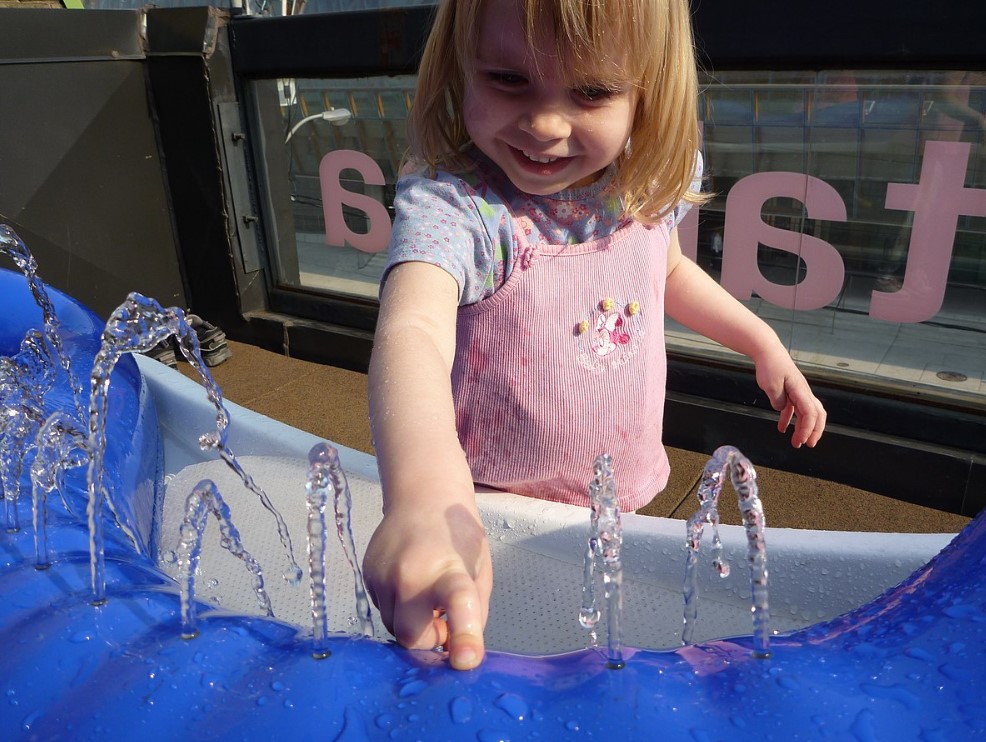 A young girl plays with small fountains of water.