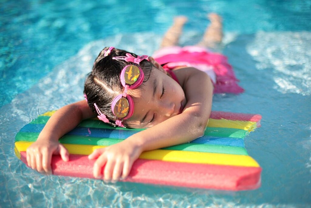 Young Asian girl lays quietly on a rainbow colored raft in a pool.