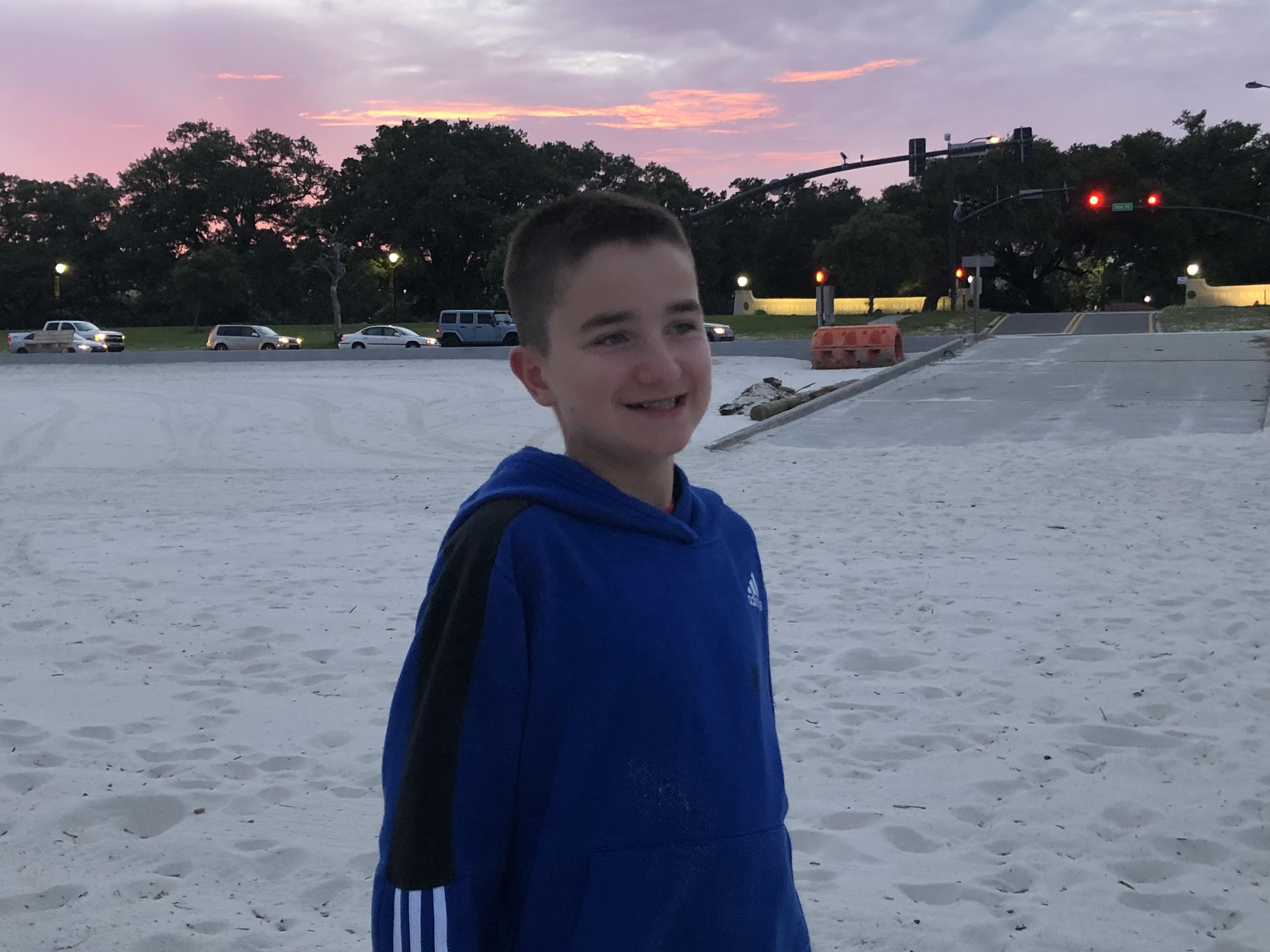 Our son smiles as he stands on the sandy beach with the sunset behind him.