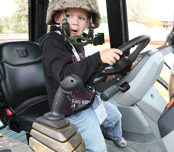 Young boy wearing a camouflage helmet operates a kid friendly backhoe.