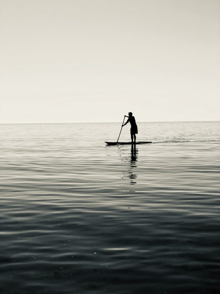 A person paddleboards on the flat waters of the ocean.