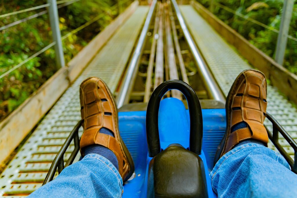 A man's feet brace the front of an alpine mountain coaster as a long stretch of track extends in front of him.