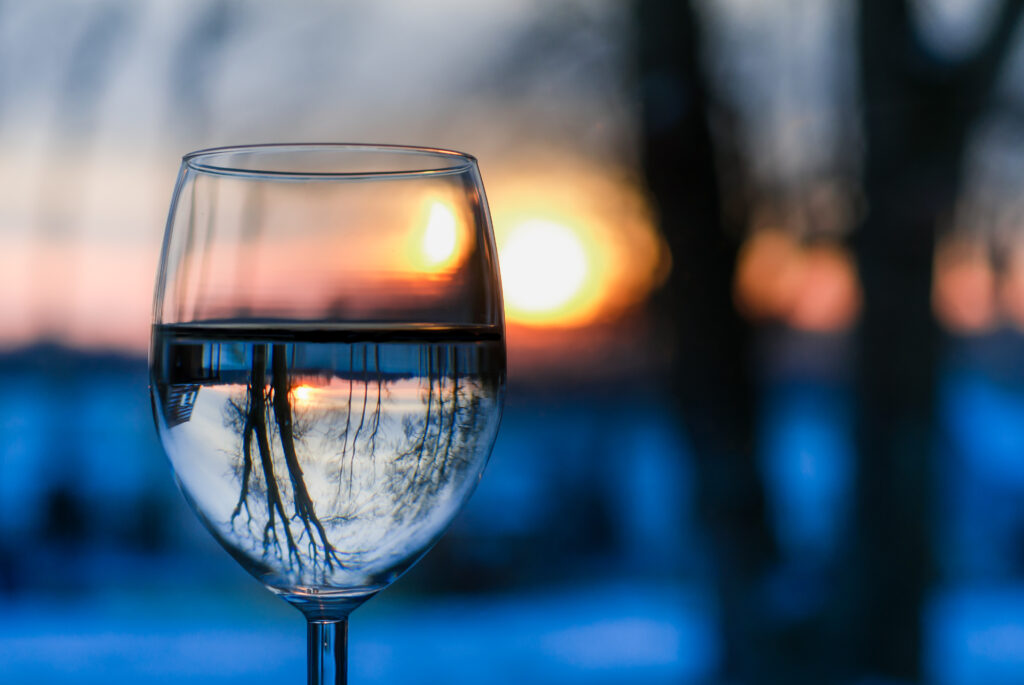 A wine glass filled with water. The landscape reflects in the water.