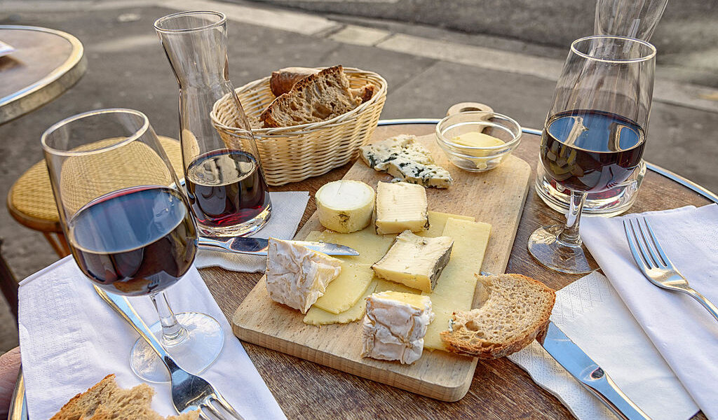 Delicious bits of cheese and bread lay on a cutting board with two glasses of red wine on either side showcasing the enjoyment of the wineries in Hocking Hills