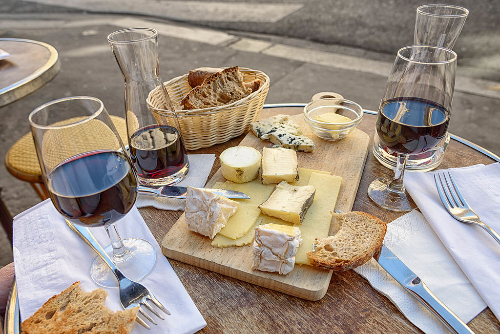 Delicious bits of cheese and bread lay on a cutting board with two glasses of red wine on either side showcasing the enjoyment of the wineries in Hocking Hills