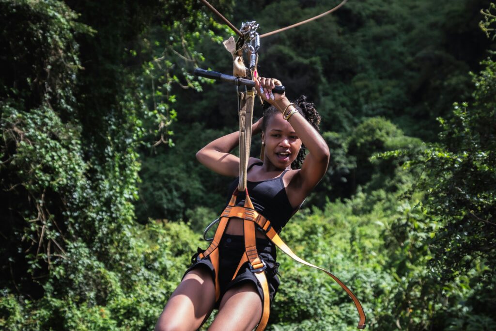 Woman holds on with one hand as she glides from high above through the trees.