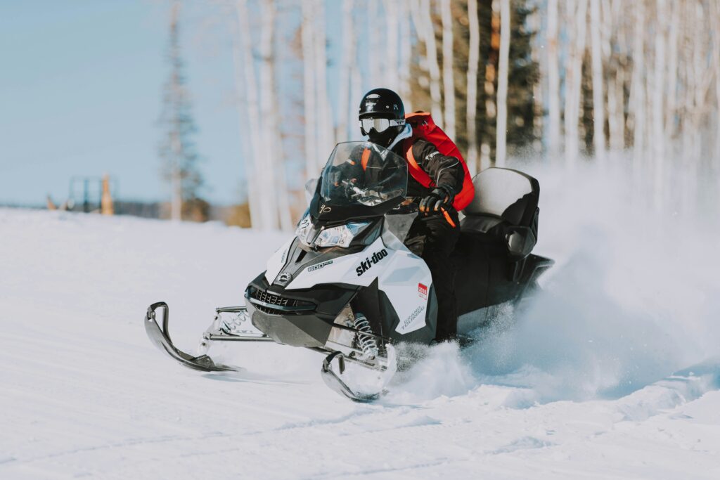 A rider wearing a red ski jacket and black helmet and goggles rides a white snowmobile in fresh powdery snow.