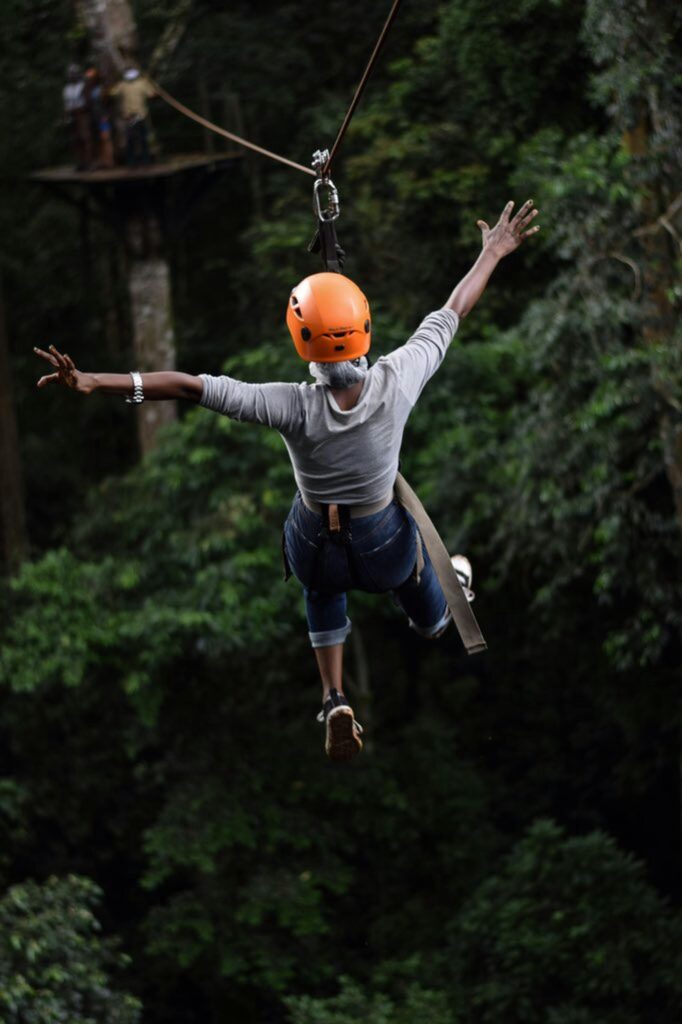 A woman excitedly glides through the treetops with both hands in the air.