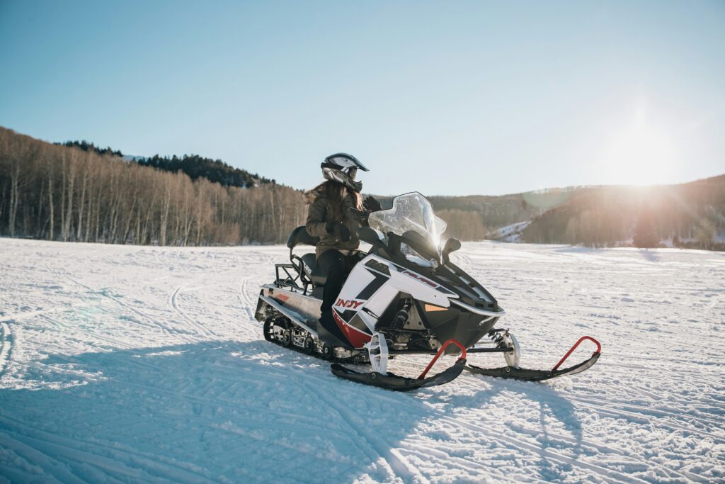 A woman enjoys a sunny day riding her snowmobile across the snowy open field.